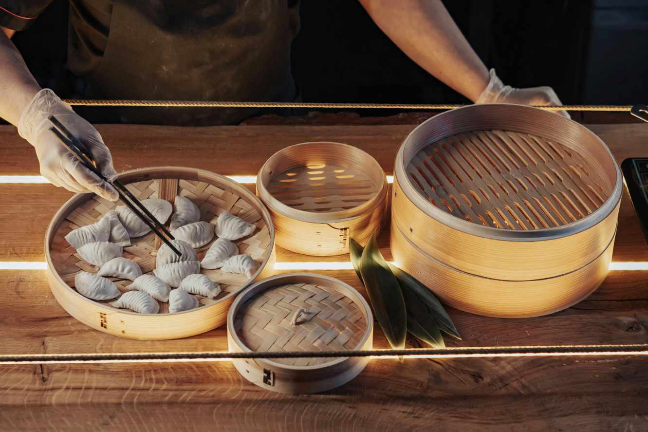 Chef preparing Cantonese dim sum dumplings in bamboo steamers with chopsticks