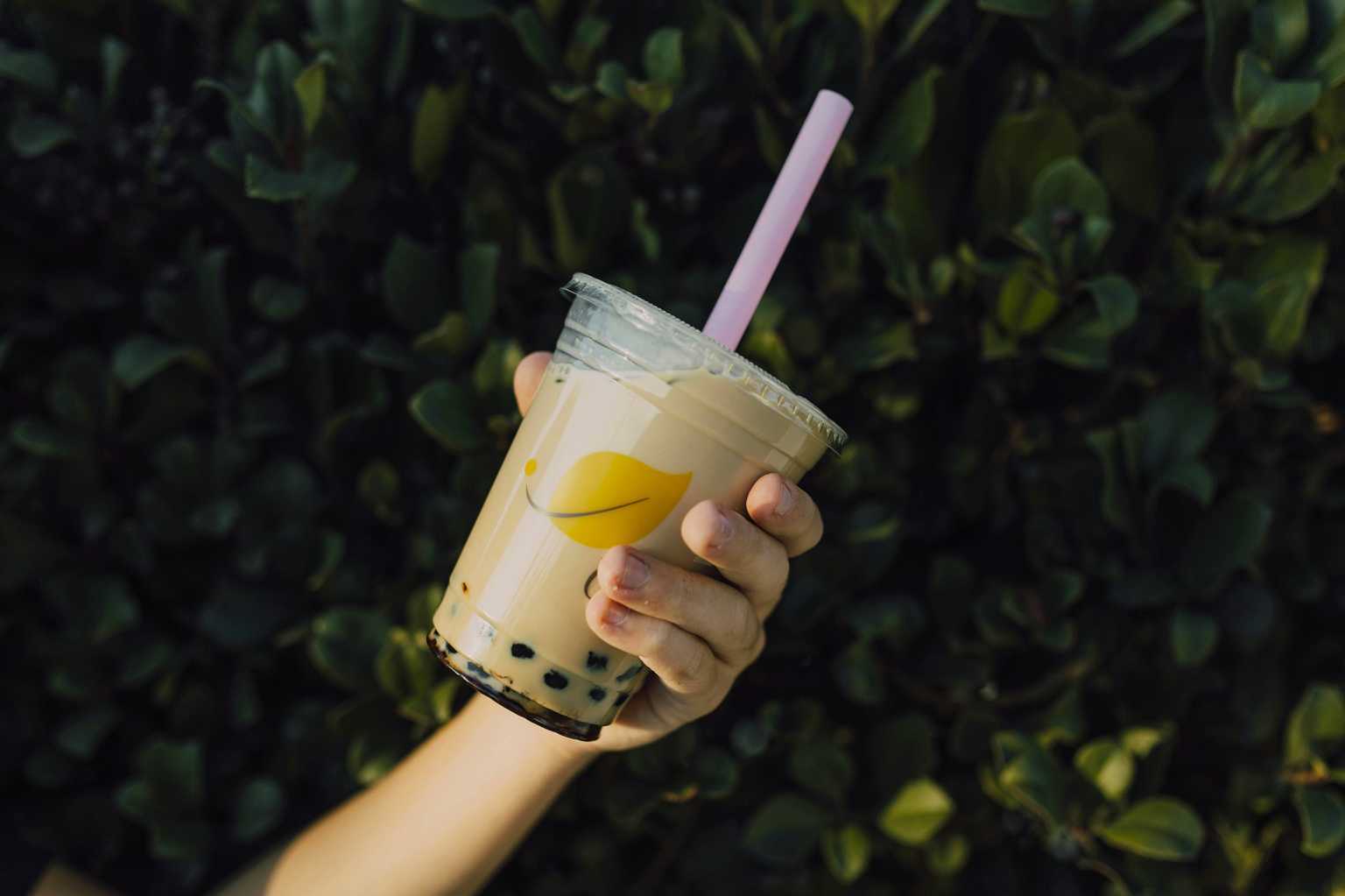 Hand holding a cup of Hong Kong-style milk tea with boba pearls outdoors