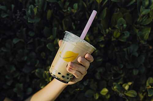 Hand holding a cup of Hong Kong-style milk tea with boba pearls outdoors
